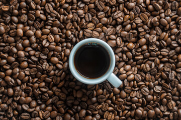 White cup of hot black coffee with a background of fresh roasted coffee beans, top view