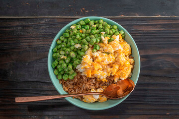 Egg fried rice and bean in green bowl on wood table.