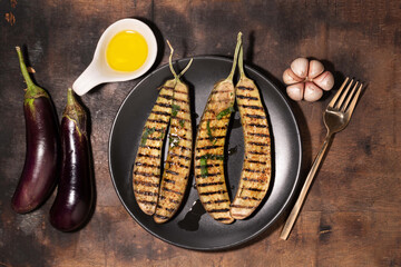 Grilled eggplants in black plate on wood background.