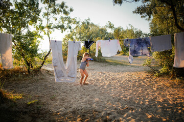 Girl child in bathing suit runs among the clothes dryer. Linen and clothes are dried on rope among...