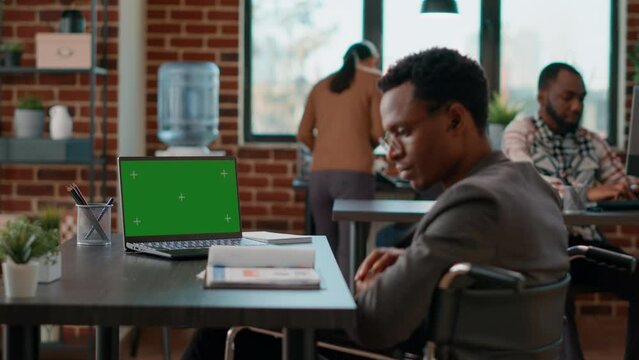 Company employee analyzing greenscreen on laptop, working in disability friendly office. Businessman using chromakey background with isolated copyspace and blank mockup template.