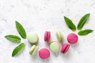 Design of green and pink macarons with mint leaves on white background. Traditional French sweet dessert.