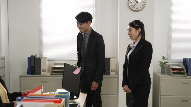 asian male manager introducing young intern to a colleague with hand gesture on first day at work in the office. the friendly female welcomes the newcomer