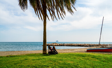 Young woman sitting under a palm tree on the beach
