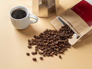 Cup of freshly brewed coffee and roasted coffee on a beige background. Making tasty strong coffee. Whole organic coffee beans spilled out of a brown paper bag at geyser coffee maker.
