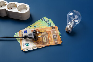 Black power plug on 50 euro banknotes and light bulb over blue background. High energy costs due to...