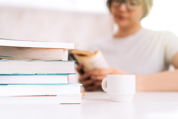 Girl with glasses reading book at table with cup of coffee.