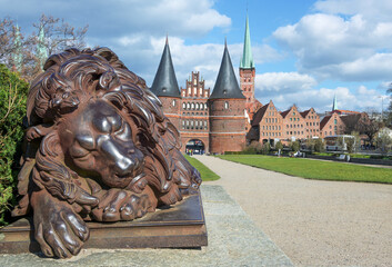 Sleeping lion sculpture from iron in front of the Holsten gate or Holstentor, the landmark of the...