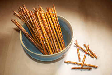 Pretzel sticks in a bowl on a wooden table, crunchy salt snack, typical served in the evening, in pubs, on a party or at home while watching TV, copy space, selected focus