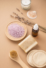 Fototapeta na wymiar Organic sea salt for the body with dry lavender flowers, sponge, brush, soap and candle on a beige background. Skin care. The concept of a natural and eco-friendly spa product