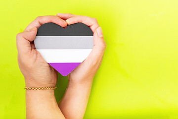 Woman hands hold heart in the colors of asexual flag on green background. LGBT concept, Pride month. Top view, copy space.