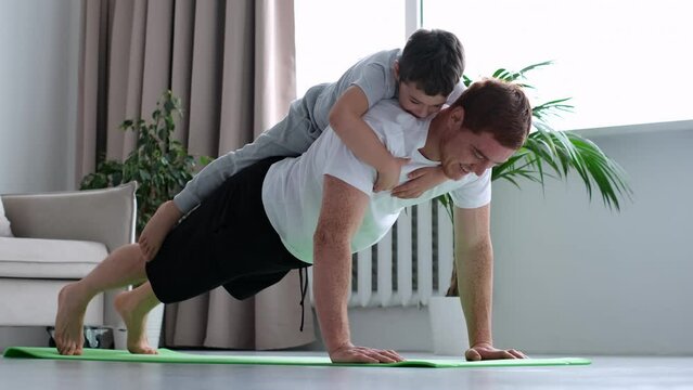 happy father doing push up exercise with son on back at gym. little boy hugs dad from behind. 4k video footage slow motion.