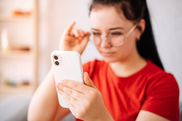 A girl with glasses with vision problems is trying to read a text on the phone at home. the girl...