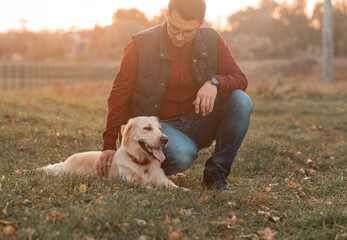 Handsome man with a dog golden retriever walk in spring meadow