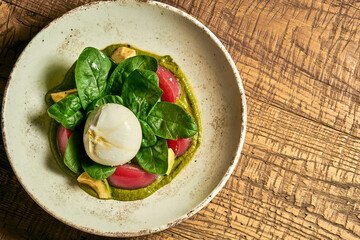 Salad with burrata, tomatoes, basil and pesto in a plate on a wooden background
