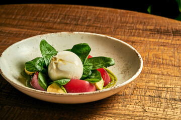 Salad with burrata, tomatoes, basil and pesto in a plate on a wooden background