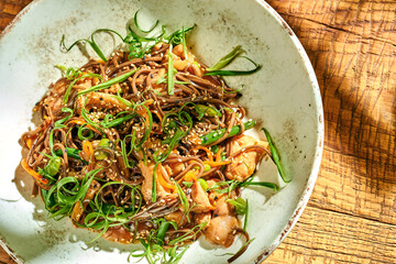 Buckwheat noodles wok in teriyaki sauce with chicken in a plate on a wooden background.