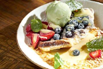 Belgian waffles with ice cream and fruit in a bowl on wooden background