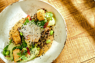 Fried tofu with quinoa and curry sauce in a bowl on a wooden background