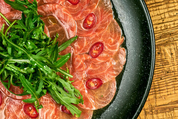 Freshly salted salmon with arugula and hot peppers in a gray plate on a wooden table. Salmon Carpaccio
