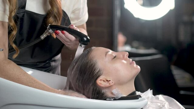 Female stylist in salon washes client head after dyeing her hair in special bath. Creating hairstyle and new fashionable image for client. process of washing hair in barber shop. girl in beauty salon