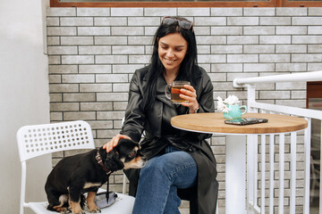 beautiful girl model eats in a cafe on the street with a black dog. hugs, loves. light background