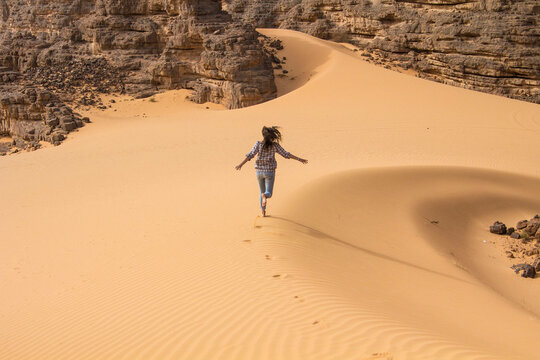 Young woman running in dunes of Sahara desert, Hoggar mountains, Djanet, Algeria