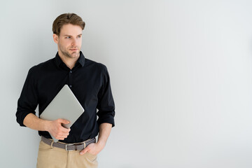 man in black shirt holding laptop while standing with hand in pocket isolated on grey.