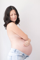 happy pretty woman enjoying pregnancy. mother to be is expecting parent. cute big tummy. pregnant brunette in light room