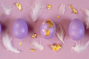 Easter greeting card with violet eggs with golden foil, white feathers on violet background.