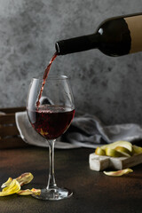 Red wine is poured into a glass on a dark gray textural background. There are pears on the board on the table.