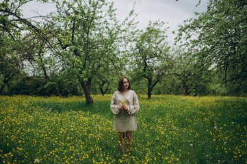 Fototapeta premium Beautiful woman in a white dress. Girl posing in the botanical garden. Around the lush grass and yellow flowers.