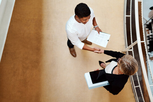 Coming together to excel together. High angle shot of two businesspeople shaking hands in an office.