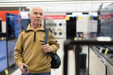 elderly man choosing TV in showroom of electronics store