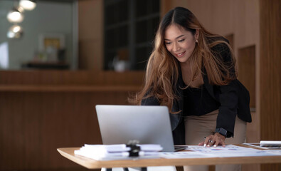 Fototapeta na wymiar Beautiful Asian businesswoman analyzes charts using laptop calculator at the office.