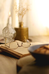 Plate of chocolate chip cookies and sugar cookies, vintage books and reading glasses, candle and flower on the table. Hygge at home. Selective focus.
