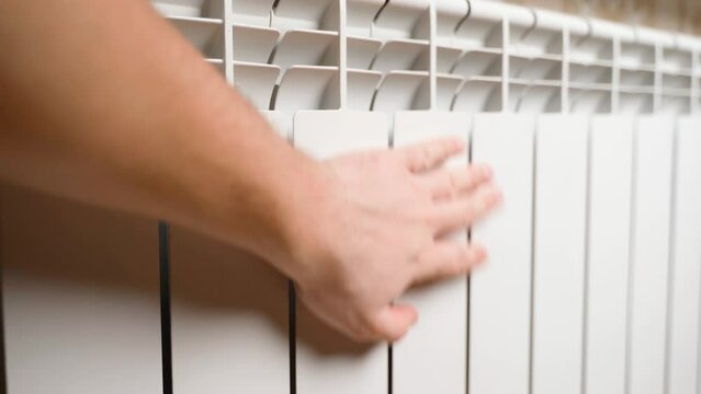 A hand touches a white battery heating radiator. Panic from turning off the heating. Bimetal aluminum heating radiator