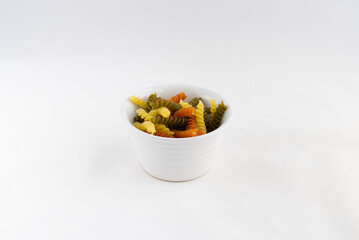 A small bowl containing multi-colored dried pasta twists (fusilli tricolori) against a white background. There is 50 grams of pasta in the bowl. Copy space all around.