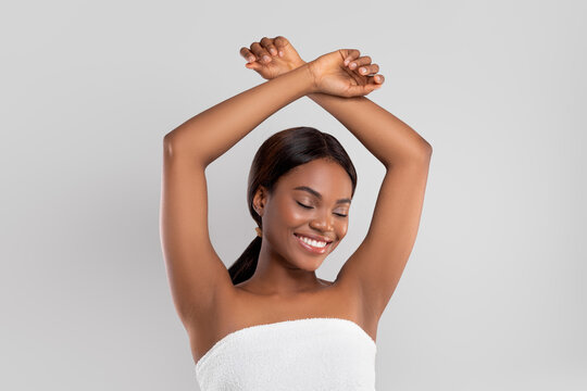 Glad pretty millennial black lady with perfect skin in towel raises hands up show armpits