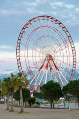 Fototapeta premium Close-up of the Ferris wheel against the background of snow-capped mountains. Beautiful city landscape, Batumi. Vertical photo