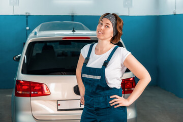 Portrait of a young smiling female mechanic plus sized in overalls posing against the background of...