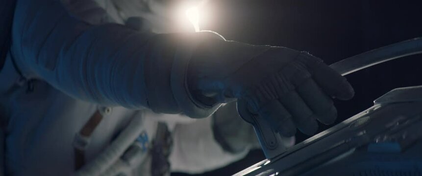 Close up on hand - astronaut performing spacewalk, working on a outer part of a space craft. Space exploration, Mars mission. Shot with 2x anamorphic lens