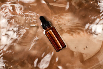 Botella de gotero con aceite esencial flotando sobre agua y un fondo marrón. Vista superior. Copy space - obrazy, fototapety, plakaty