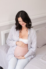 charming pregnant woman in shirt on bed. happy pregnancy