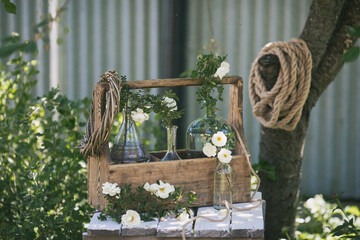 A beautiful postcard. Vintage composition of bottles and white roses on a wooden table. Summer. Processing in the style of an old movie.