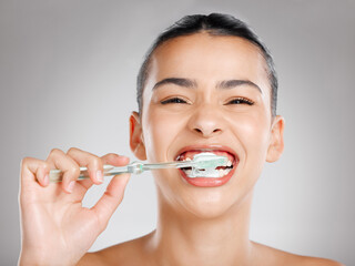 Do your dentist proud. Studio shot of an attractive young woman brushing her teeth against a grey background.