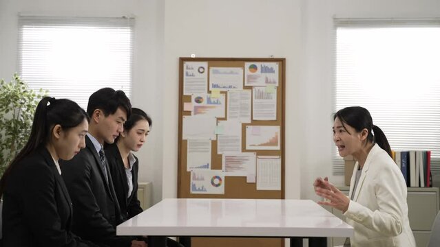 frustrated asian company staff sitting opposite and listening to angry boss shouting for bad sales performance at corporate group meeting. she pointed at the ineffective male worker