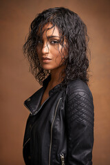 Leather and style. Studio shot of an attractive young woman in a leather jacket against a brown background.
