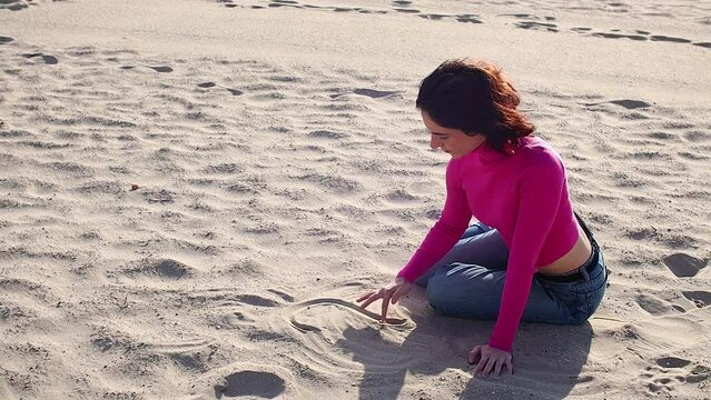 Young woman draws a heart on the sand