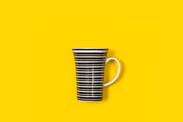 Taza de cerámica a rayas blancas y negras sobre un fondo amarillo aislado y brillante. Vista...